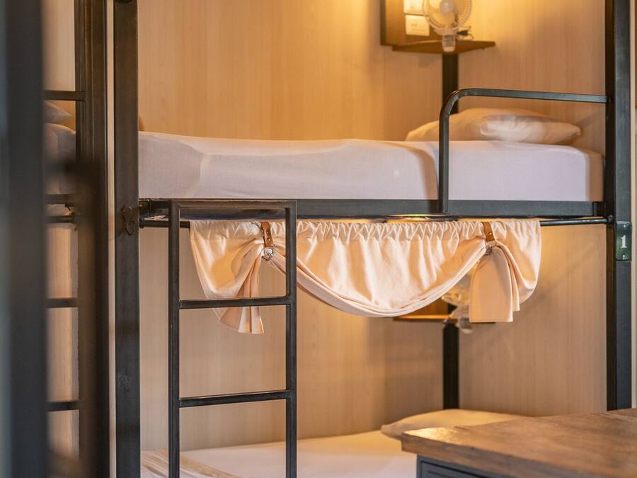 Quarto com beliche, mesa de cabeceira e luminária fixada na parede.