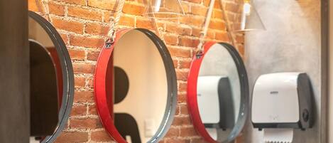 A restroom with three sinks, two round mirrors with red frames, and a brick wall.