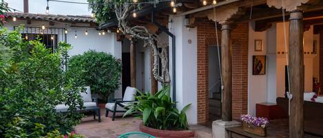 Un patio con mesas al aire libre, luces colgantes y abundante vegetación.