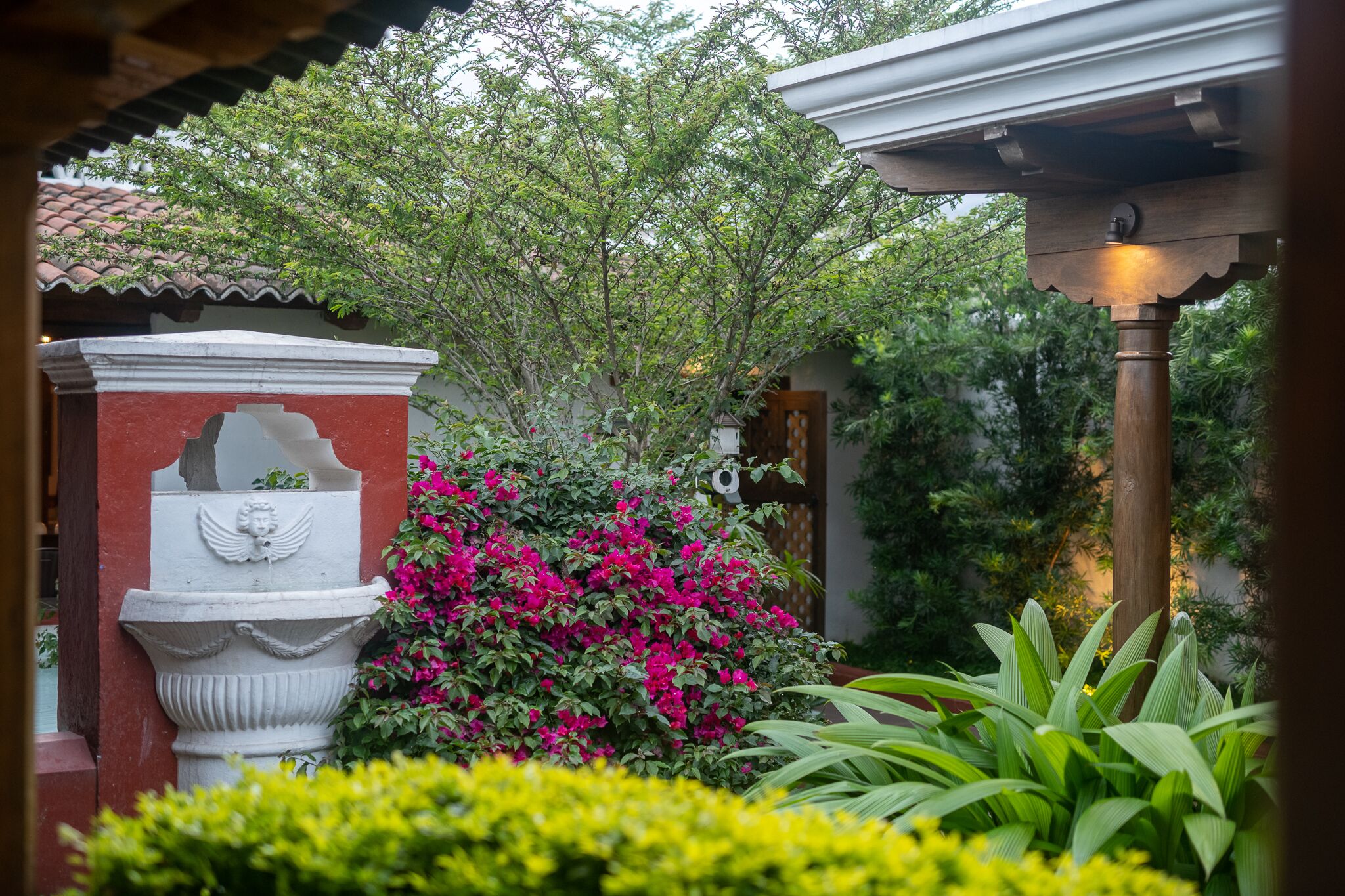 Un jardín con una fuente, abundante vegetación y una estructura de edificio tradicional.