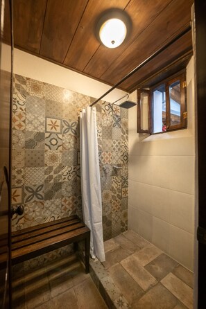Ducha con azulejos estampados, un banco de madera y una pequeña ventana con marco de madera.