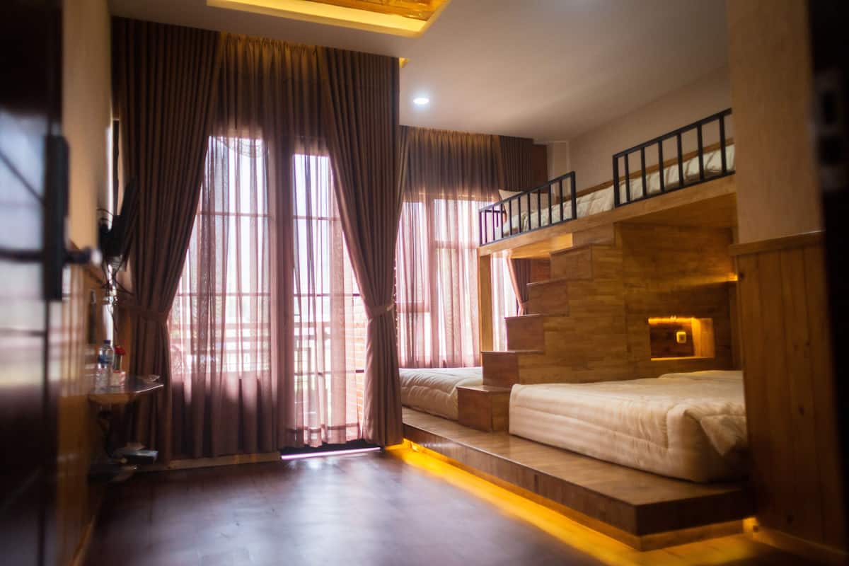 A bedroom with a bunk bed, wooden flooring, a staircase, and a large window with curtains.