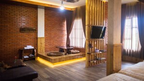 A modern room with a brick wall, wooden furniture, a flat-screen TV, and a cozy seating area. - Pariban Hotel (Berastagi)