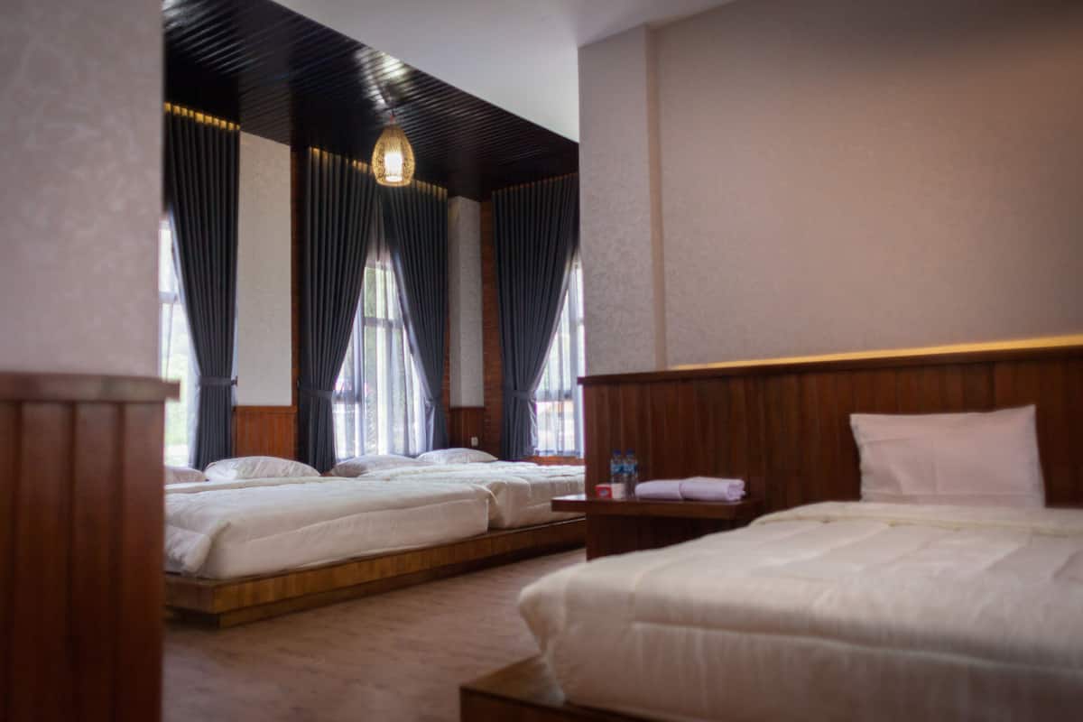 A hotel room with two beds, a wooden headboard, a bedside table with a bottle, and a hanging light fixture.