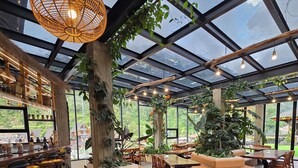A spacious indoor area with a glass ceiling, stone flooring, wooden furniture, and a bar area with stools. - Pariban Hotel (Berastagi)