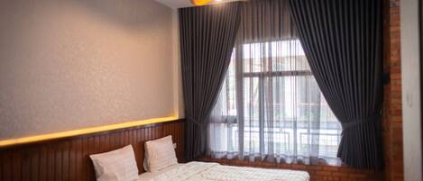 Quarto com cama grande, cabeceira de madeira e janela com cortinas.