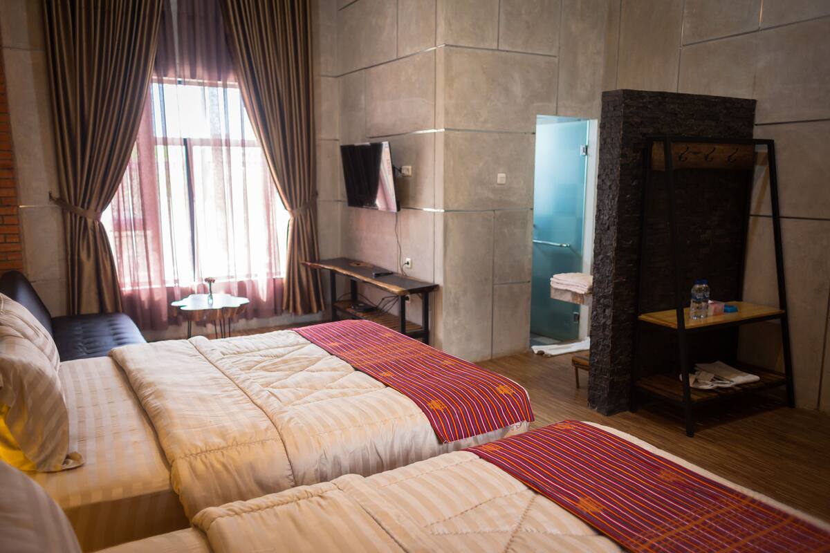A hotel room with two beds, a desk, a TV, and a bathroom.
