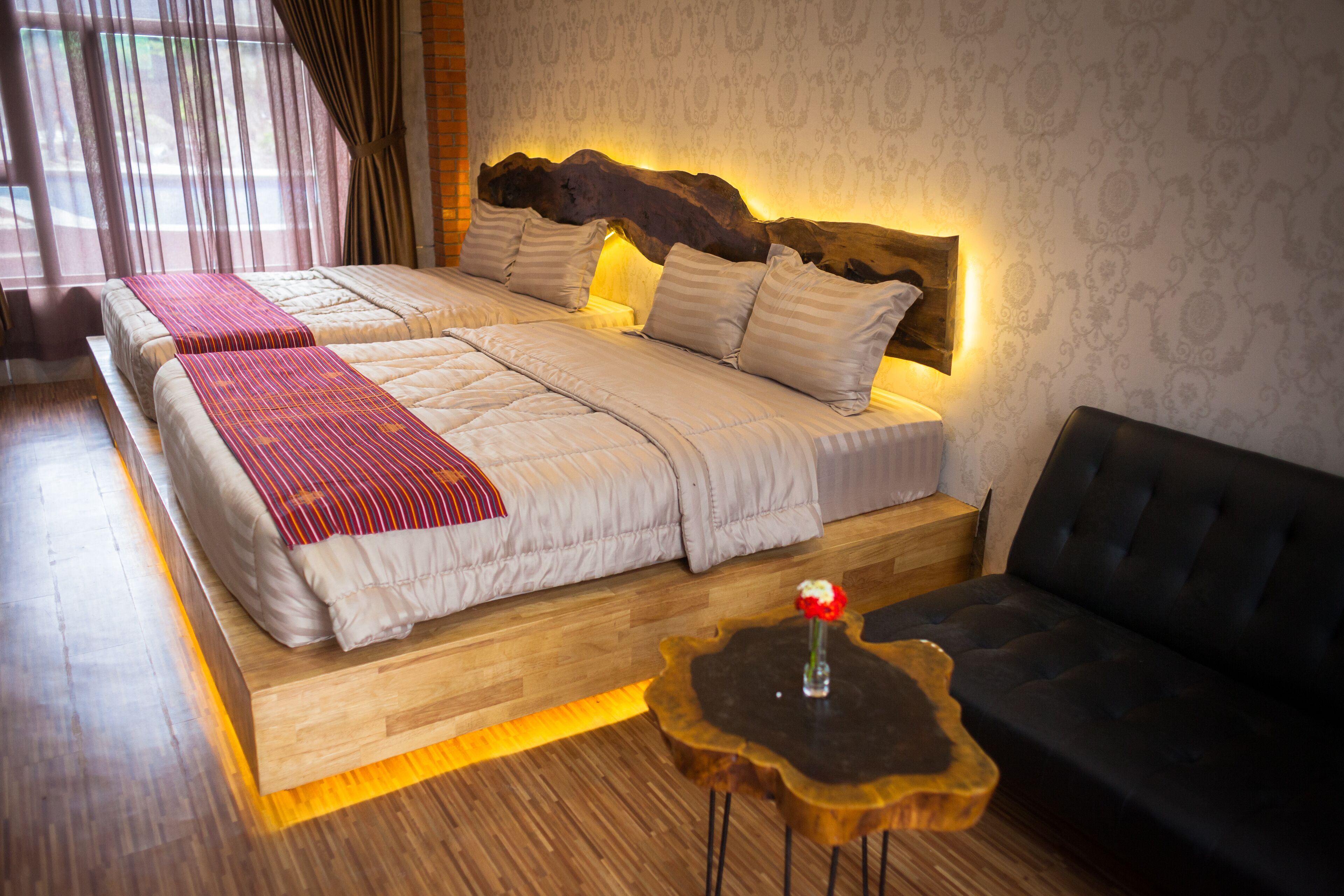 Une chambre d’hôtel avec un grand lit, une tête de lit en bois, une petite table avec un vase et un canapé noir.