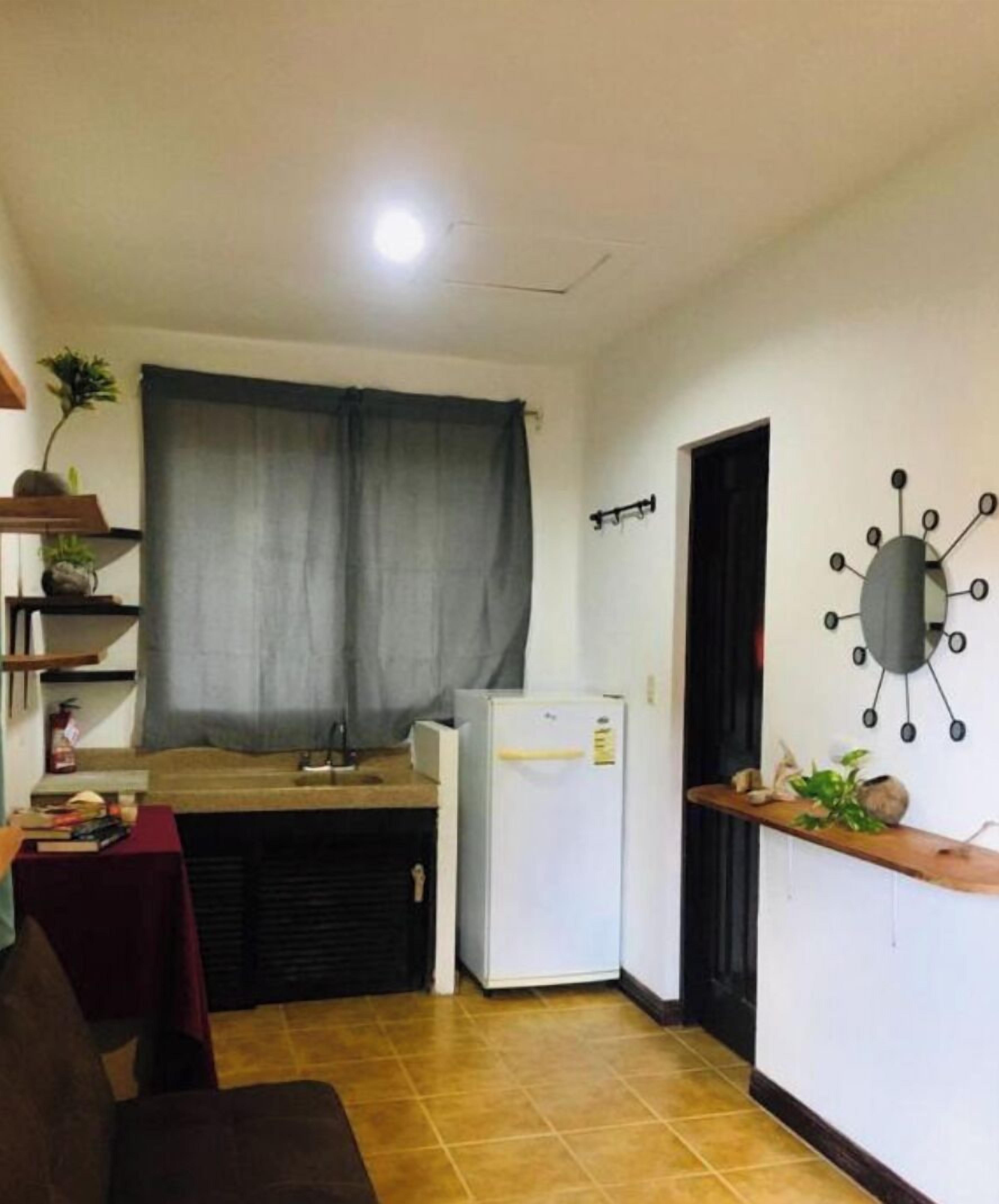 Eine kleine Küche mit einem Kühlschrank, einem Esstisch und einem Fenster mit Vorhängen.