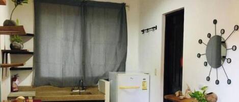 Eine kleine Küche mit einem Kühlschrank, einem Esstisch und einem Fenster mit Vorhängen.
