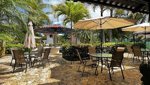 Une terrasse extérieure avec un sol en pierre, des tables, des chaises et des parasols.