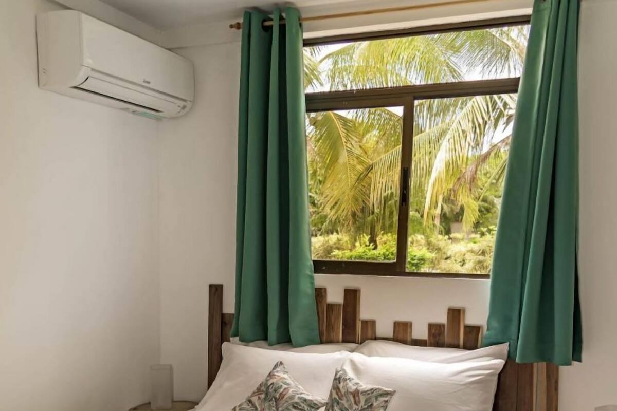 Una cama con colcha estampada, dos almohadas y cortinas verdes.