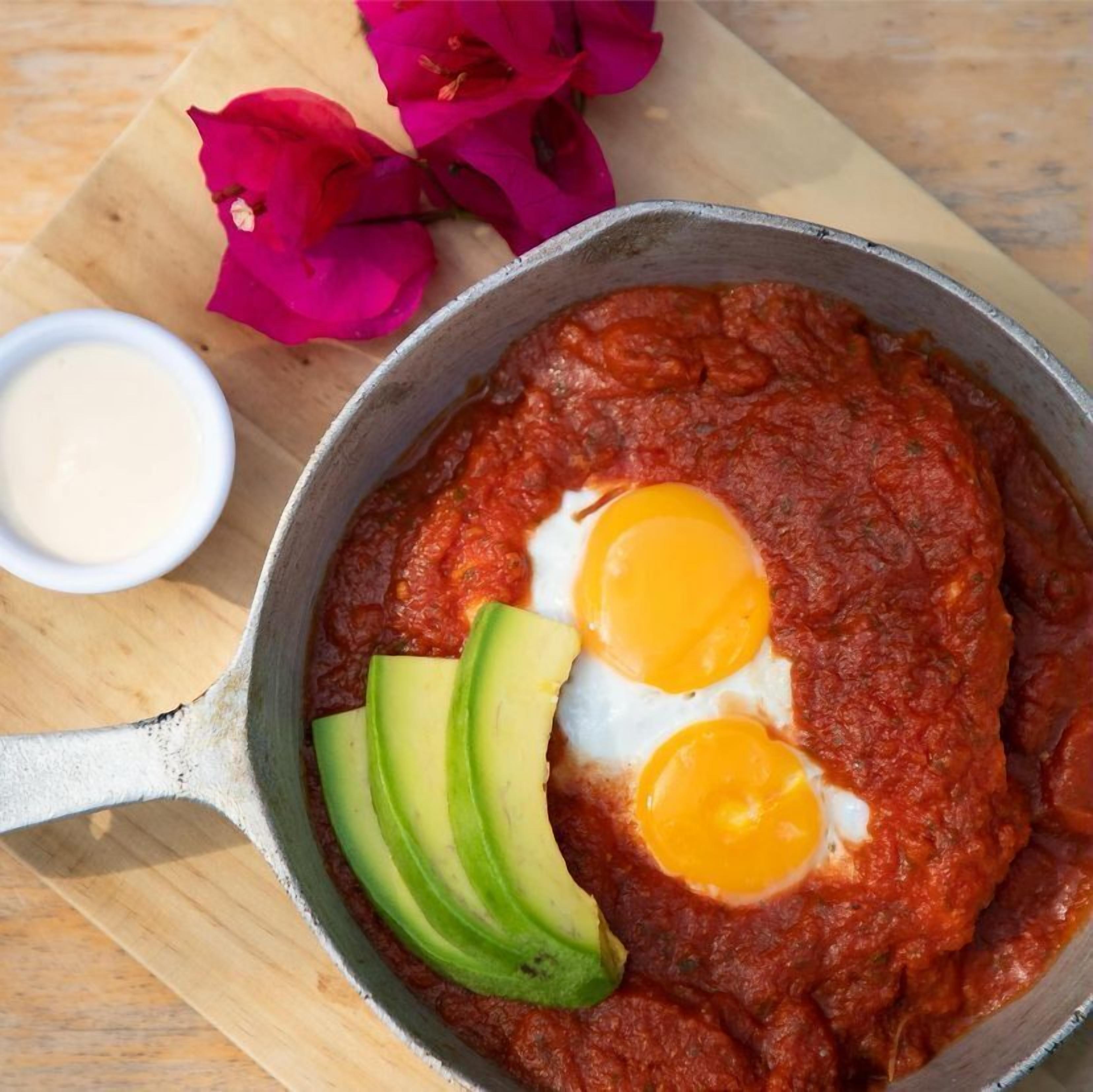 Una sartén con huevos y aguacate sobre una tabla de madera.