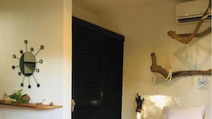 Une chambre à coucher avec un lit, une tête de lit en bois, une horloge murale, une étagère avec des plantes et une porte.