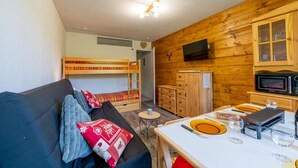 A cozy room with a bunk bed, a sofa, a dining table with plates and glasses, a microwave, and a TV on the wall. - L'Igloo - Studio pour 4 vue montagne (Villarembert)