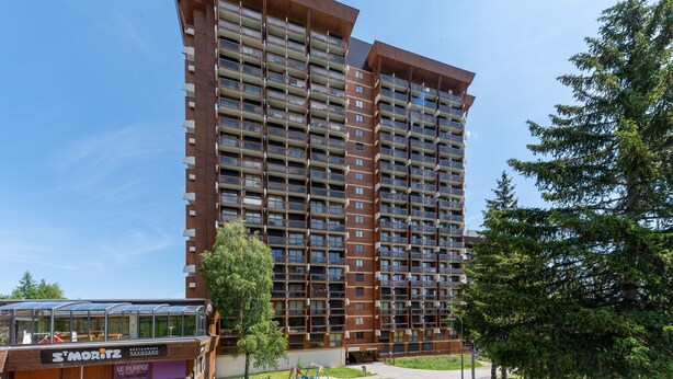 A high-rise building with multiple balconies, a restaurant named "St. Moritz" at the base, and surrounding greenery. - L'Igloo - Studio pour 4 vue montagne (Villarembert)