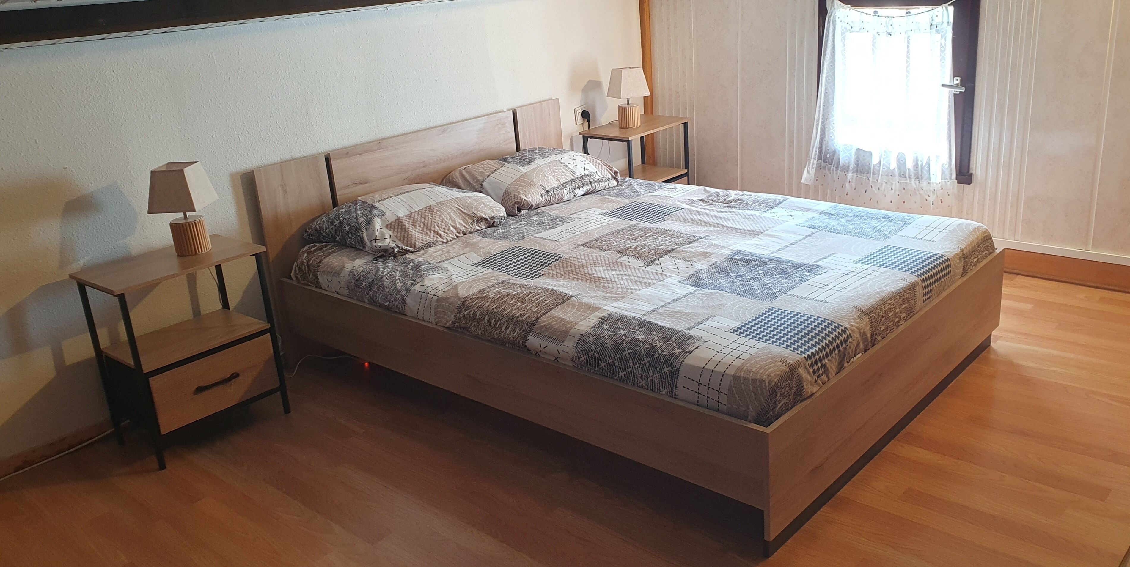 Une chambre à coucher avec un lit en bois, deux tables de chevet, une lampe sur chacune, et une fenêtre avec des rideaux.