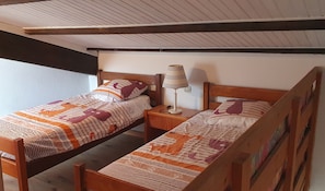 A room with two wooden beds, each with a patterned bedspread and pillows. There is a nightstand with a lamp between the beds. - L'Azur - Maison avec terrasse proche plage (Le Barcarès)