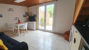 Cozinha compacta com área de refeições, um sofá com almofada amarela e uma porta de vidro deslizante para área externa.