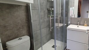 Casa de banho moderna com cabine de duche em vidro, sanita branca e toucador com espelho.