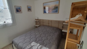 Quarto com cama, cabeceira de madeira, janela com cortinas e guarda-roupa de madeira com cabides.