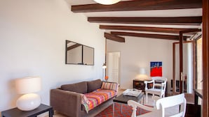 Ein Wohnzimmer mit braunem Sofa, einem Couchtisch, einer Lampe, einem bunten Teppich und einem weißen Sessel.