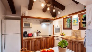 Une cuisine avec des armoires en bois, un four à micro-ondes, une cuisinière et un évier. On peut voir un panier de tomates sur le comptoir et une plante dans un pot.