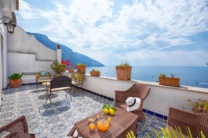 A terrace with patterned flooring, wicker furniture, potted plants, and a table with drinks. - Villa Elsa in Positano (Positano)