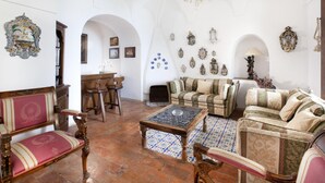 Uma sala de estar espaçosa com teto alto e abobadado, decorações elaboradas nas paredes e diversas opções de assentos, incluindo um sofá e poltronas.