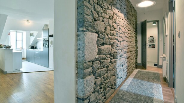 A modern kitchen with grey cabinets, a stone accent wall, and a wooden floor.