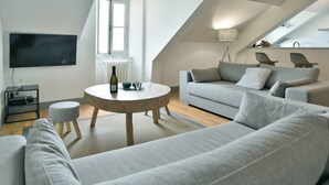 A modern living room with a grey sofa, a round coffee table, and a flat-screen TV mounted on the wall.