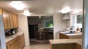 A kitchen with wooden cabinets, a dining area with a table and chairs, and a view of the outdoors through a window. - Cozy country farmhouse (Prairie City)