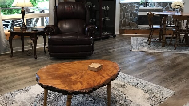 A living room with a leather chair, a wooden coffee table, a stone fireplace, and a dining area with wooden chairs. - Cozy country farmhouse (Prairie City)