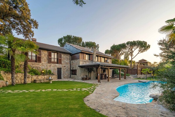 Une maison en pierre avec une piscine, un patio couvert et une pelouse bien entretenue.