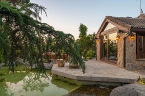 A stone building with a tiled roof, a pond, and surrounding greenery. - Chalet de lujo Arroyomolinos (Batres)