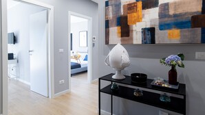Een modern interieur met een gang die naar een slaapkamer leidt, een zwarte console tafel met decoratieve objecten, en een groot abstract schilderij aan de muur.
