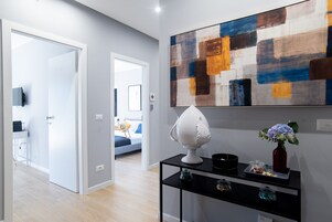 Ein modernes Interieur mit einem Flur, der zu einem Schlafzimmer führt, einem schwarzen Konsolentisch mit Dekoration und einem großen abstrakten Gemälde an der Wand.