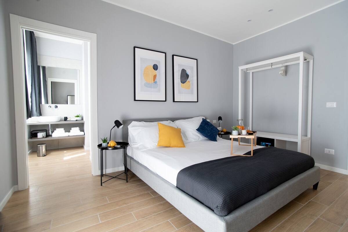 Een moderne slaapkamer met een groot bed, een nachtkastje, een spiegel en twee ingelijste kunstwerken aan de muur.