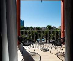 Ein Balkon mit zwei schwarzen Stühlen und einem kleinen Tisch, mit Blick auf eine Skyline mit Palmen und Gebäuden.