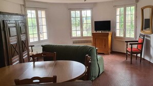 Ett rum med ett träbord, en grön soffa, ett träskåp, en tv, en stol och ett kylskåp.
