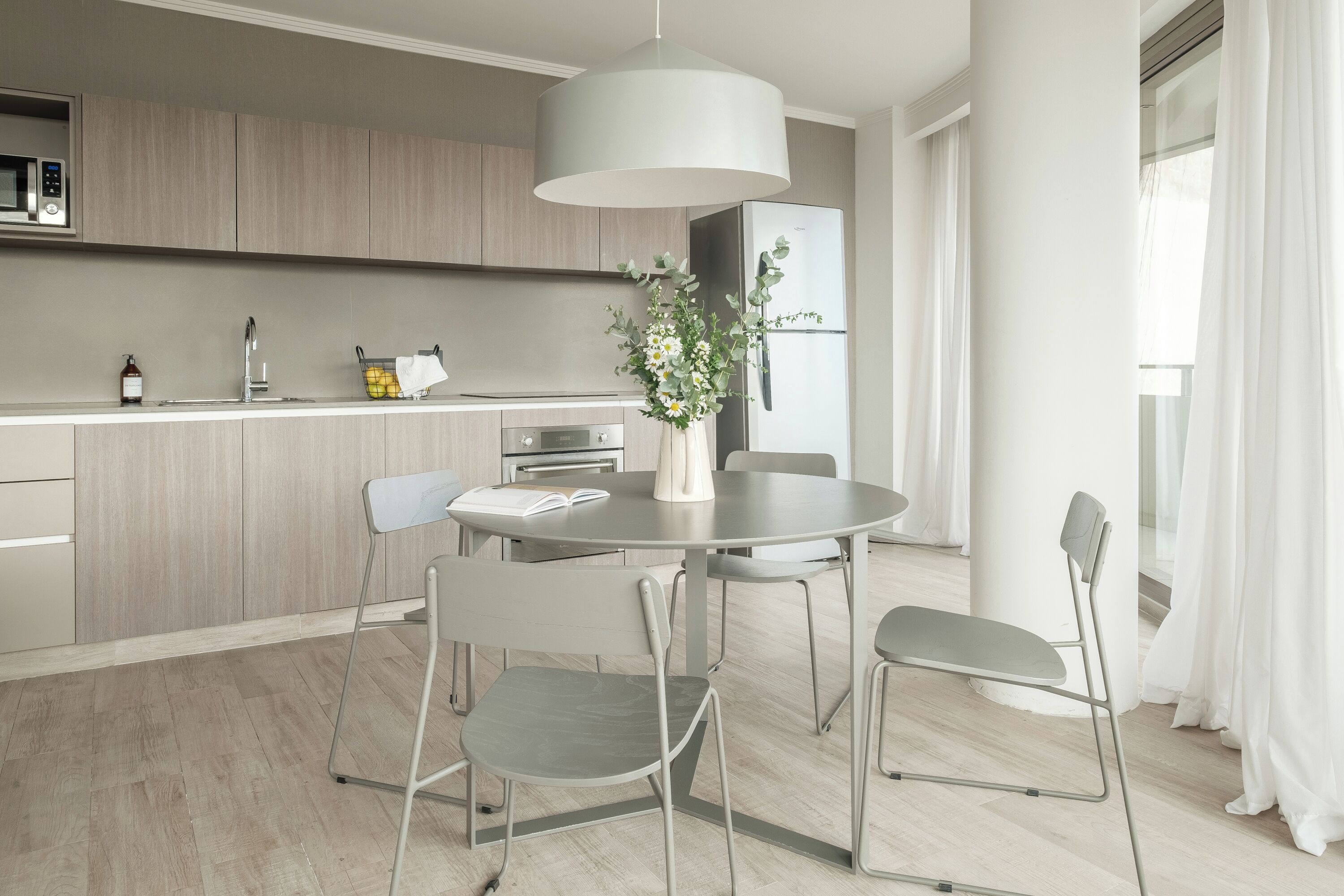 Eine moderne Küche mit Essbereich, ausgestattet mit einem runden Tisch, vier Stühlen, einer Pendelleuchte und einem Kühlschrank.