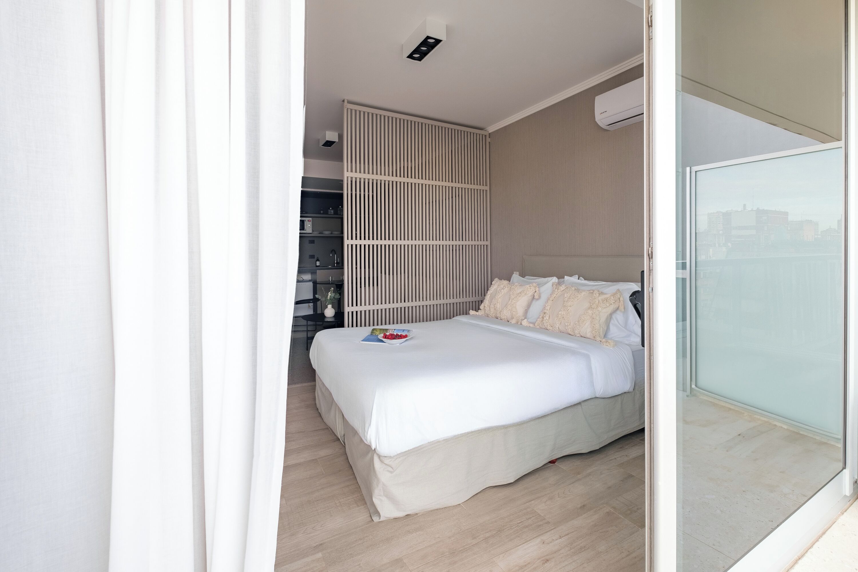 A modern bedroom with a large bed, a wardrobe, and a view of the city through a sliding door.
