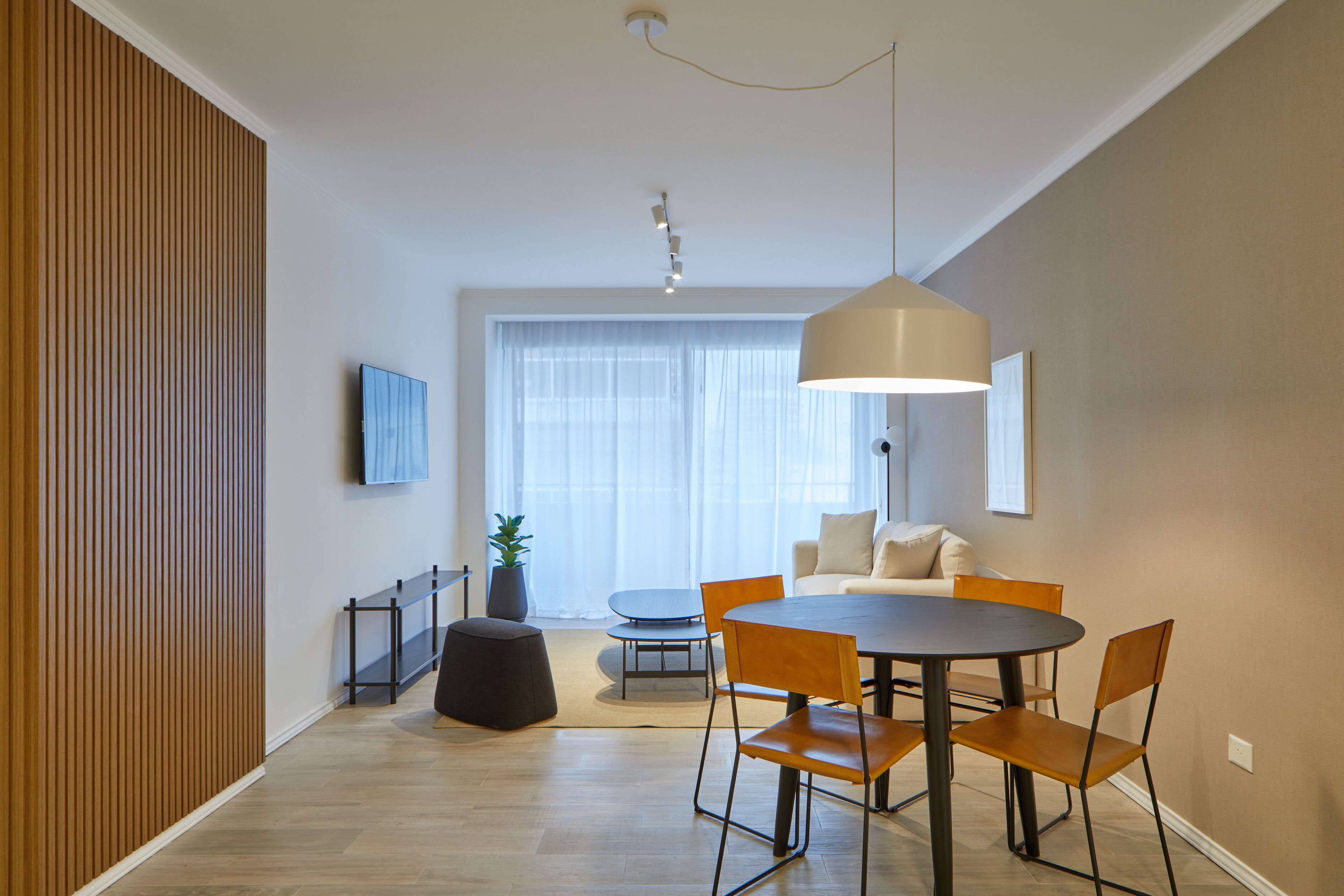 A modern dining area with a round table, four chairs, a pendant light, and a potted plant.