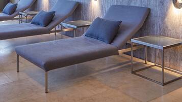 Filas de sillones de descanso con estructura metálica y cojines grises, ubicados frente a una pared texturizada con iluminación integrada.