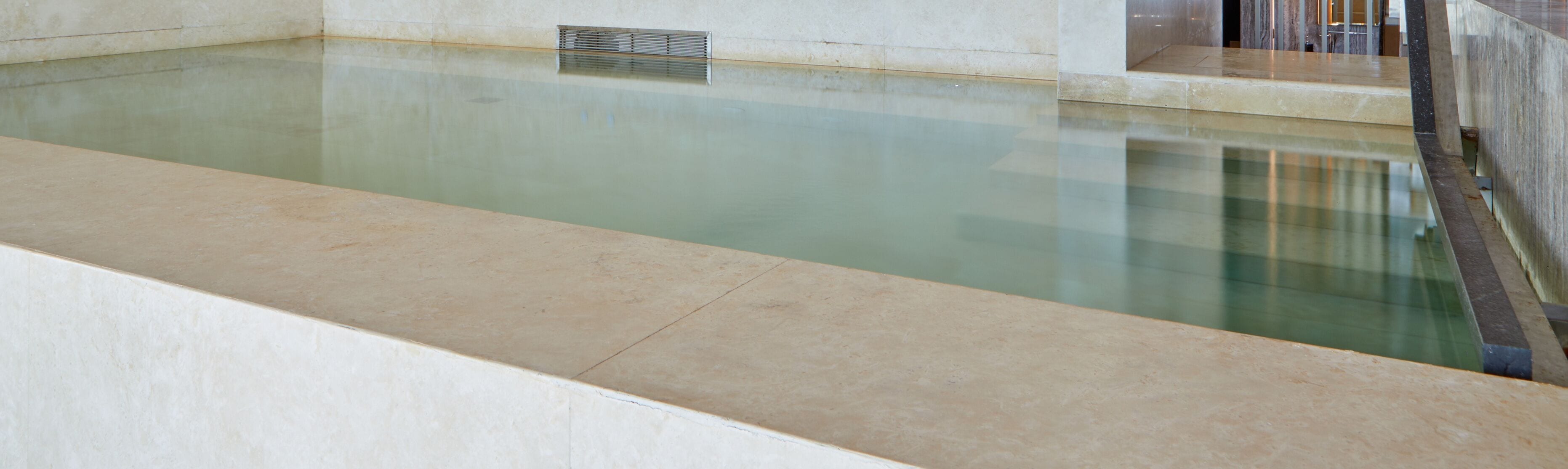 A swimming pool with a tiled edge and a metal vent on the wall.
