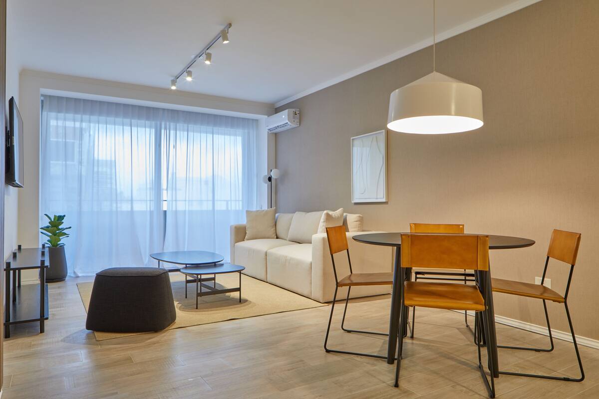 Una sala moderna con comedor, un sofá, una mesa de centro e iluminación colgante.