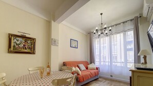 Ein gemütliches Zimmer mit Esstisch, Stühlen, einer Couch, einer Chandelierleuchtre und einem fenster mit Vorhängen.