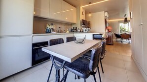 A modern kitchen with white cabinets, a dining table with chairs, and pendant lighting. - N&J - FLEURS TERRASSE - 3 bedrooms (Niza)