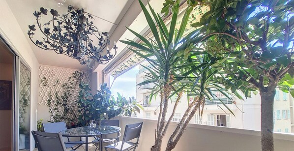 A balcony with a glass table and chairs, surrounded by potted plants and a decorative metal chandelier.