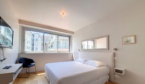 A bedroom with a bed, a desk, a chair, a window, and a mirror.